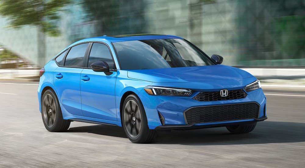 Blue 2026 Honda Civic Hatchback driving down a city street.