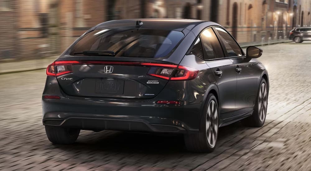 Rear of a black 2026 Honda Civic Sport Touring Hybrid driving down a city street.