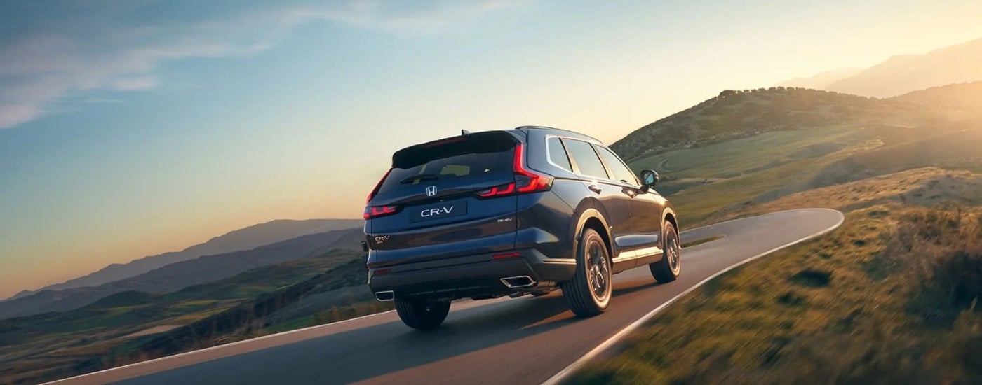 Rear of a dark blue 2026 Honda CR-V Hybrid driving around a bend.