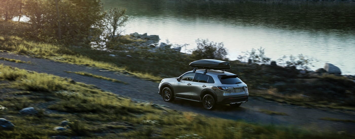 Rear of a grey 2026 Honda HR-V Sport driving off-road by a lake.