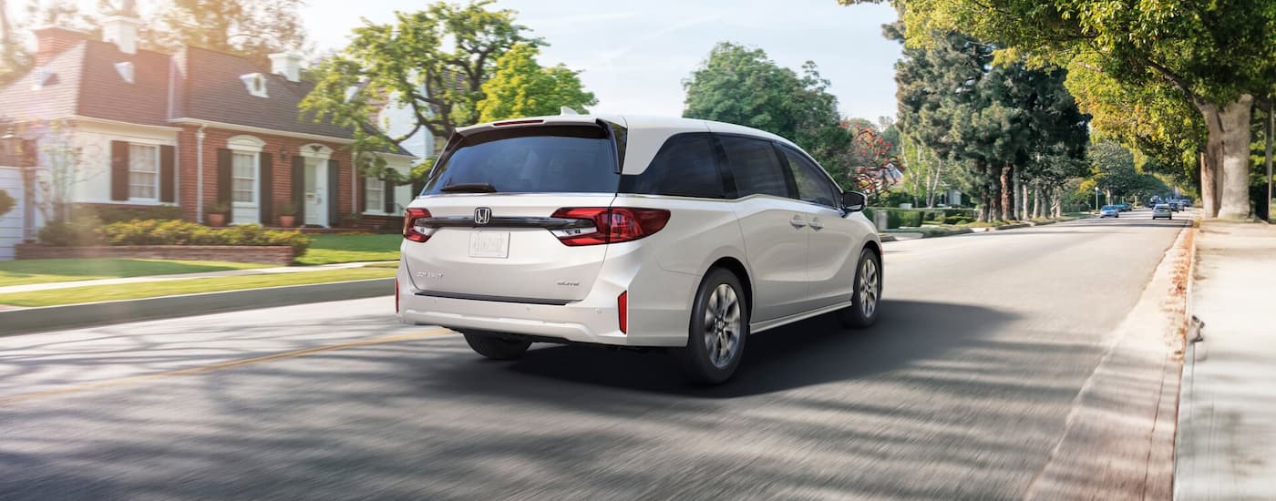 Rear of a white 2026 Honda Odyssey driving down a neighborhood street.