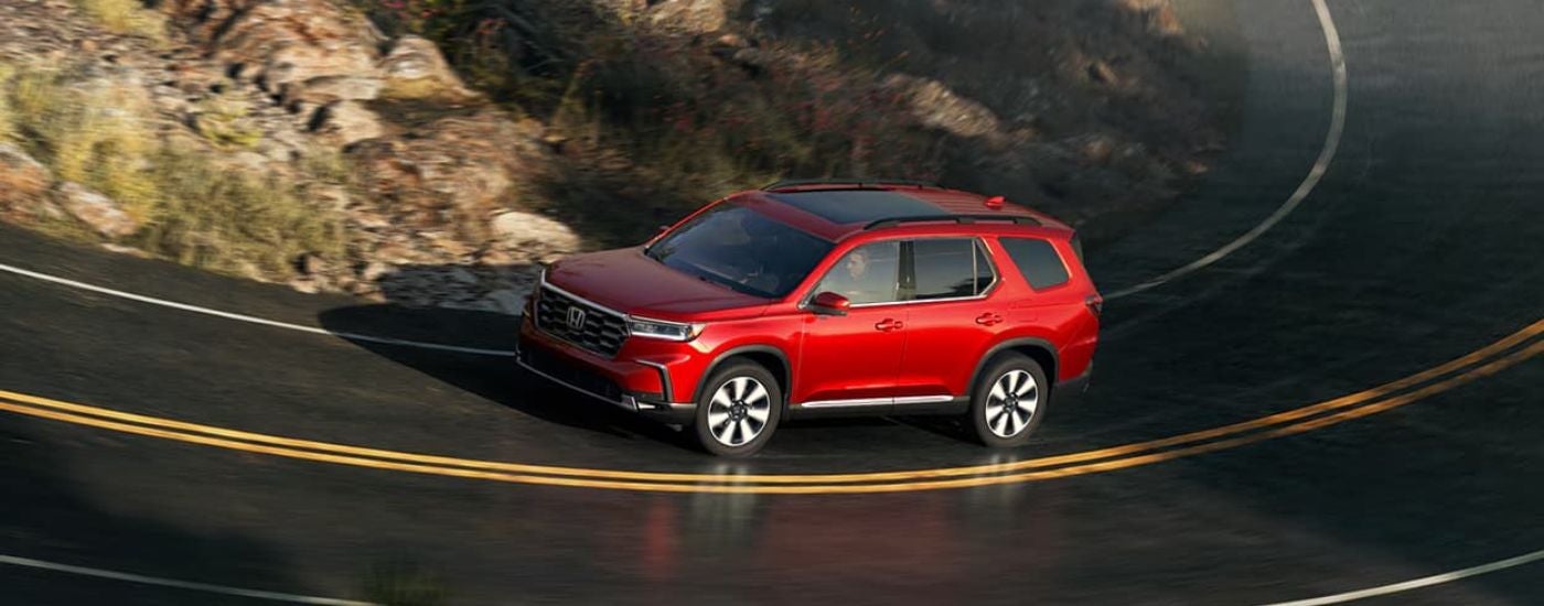 Red 2026 Honda Pilot driving around a bend.