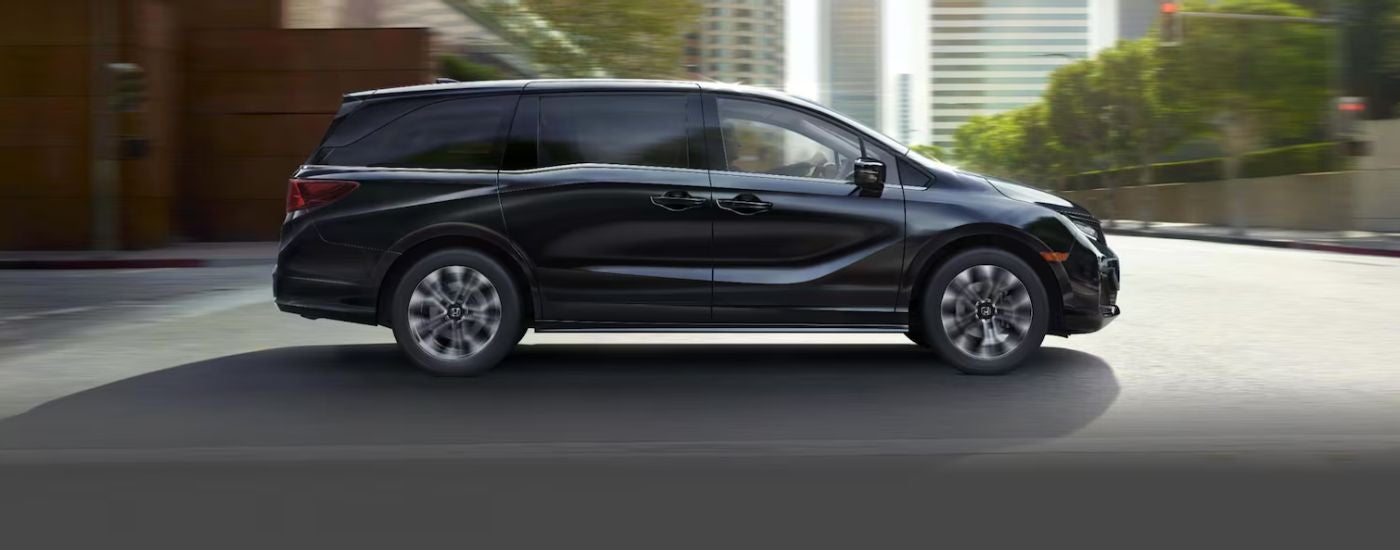Black 2026 Honda Odyssey driving down a road in the city.