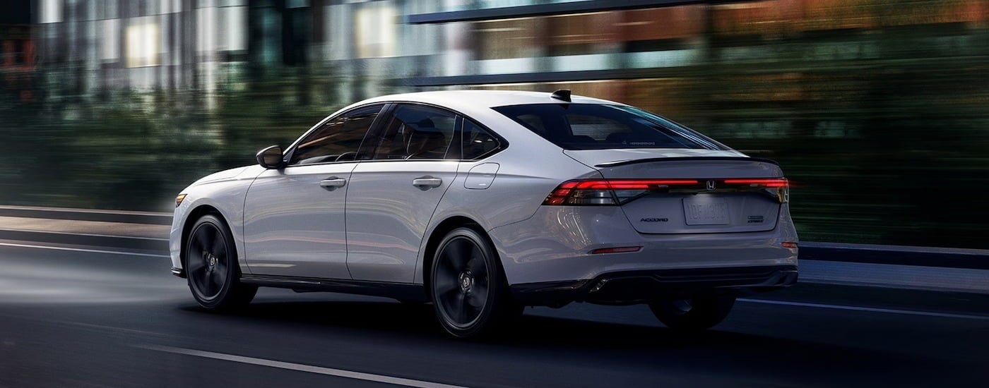 Rear of a white 2026 Honda Accord Hybrid driving down a road.