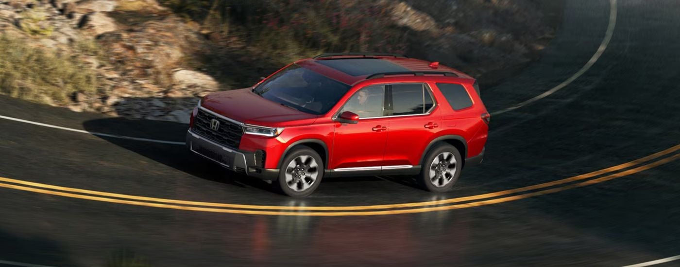 Red 2026 Honda Pilot driving around a bend in the road.