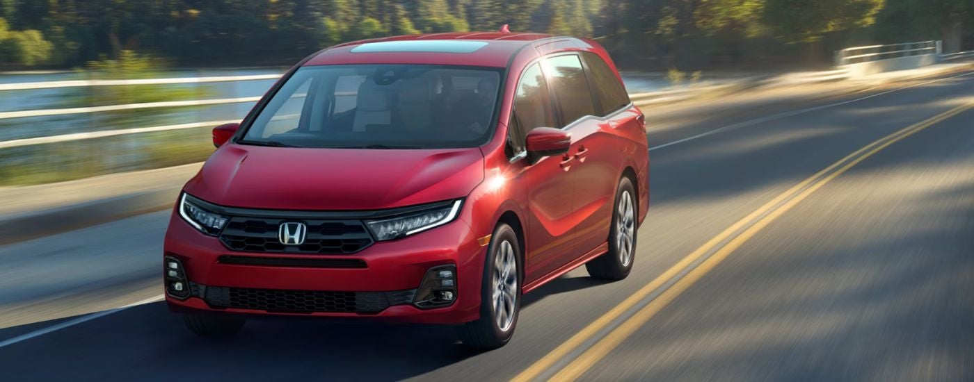 Red 2026 Honda Odyssey driving on a road near a lake.