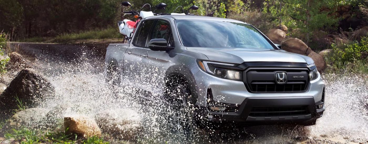 Silver 2026 Honda Ridgeline driving through a river with dirtbikes in the bed.