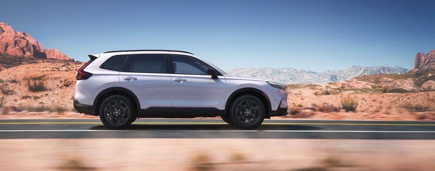 White 2026 Honda CR-V Sport driving on a paved desert road.