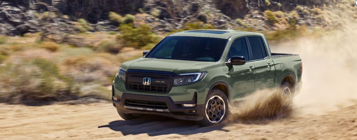 A green 2026 Honda Ridgeline driving on a sand-lined road.