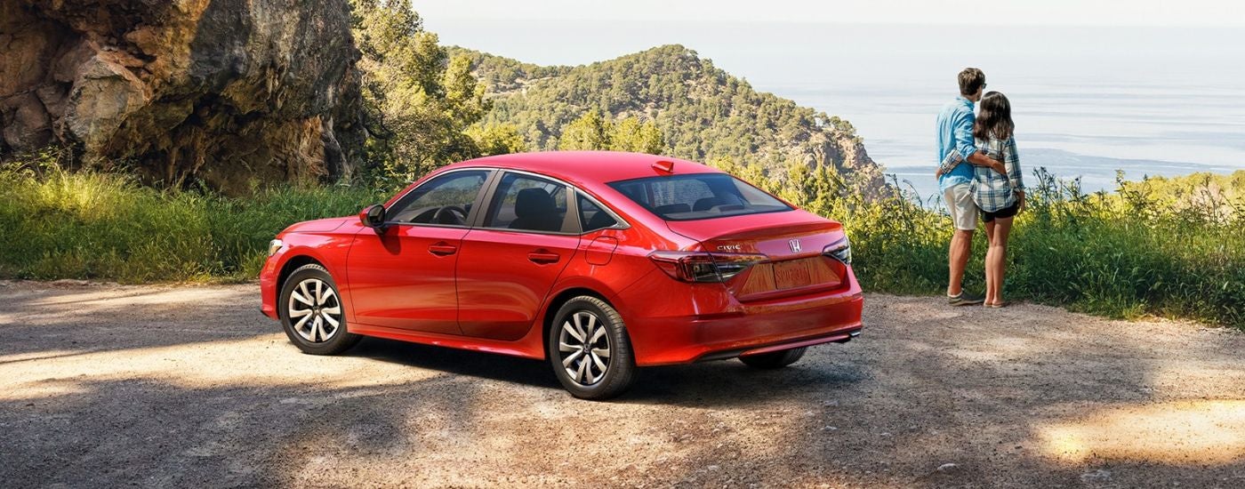 Red 2026 Honda Civic Sedan parked by a scenic view and two people.
