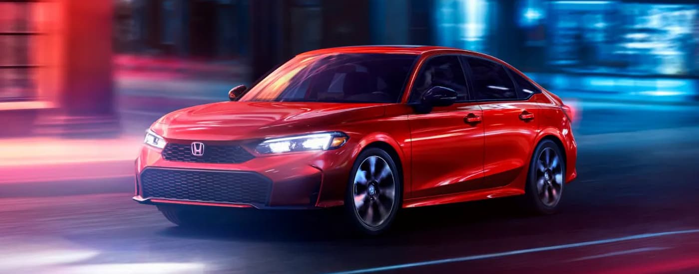A red 2025 Honda Civic driving down a city street at night 